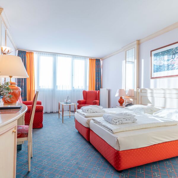 Helles Zimmer mit rotem Doppelbett und hellem Kopfteil unter einem Gemälde